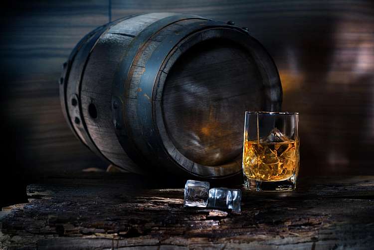 A glass of whiskey with ice on background barrel